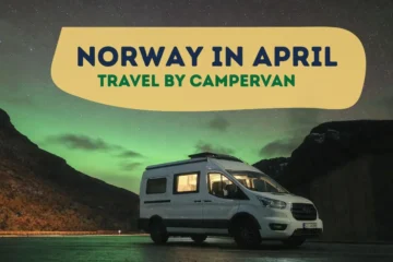 White campervan parked under the Northern Lights in Norway in April, surrounded by mountains at night